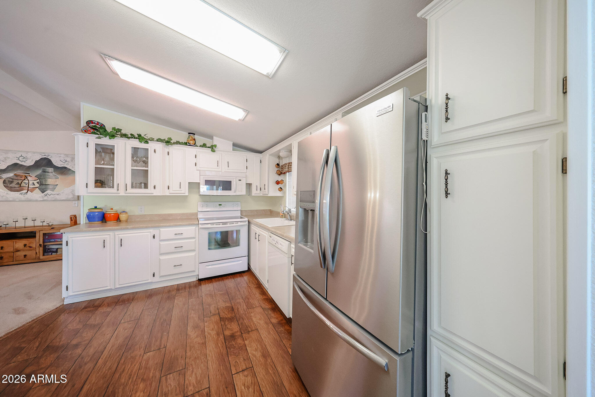 Kitchen with white cabinets, stainless steel refrigerator, white range, and warm wood-look flooring.