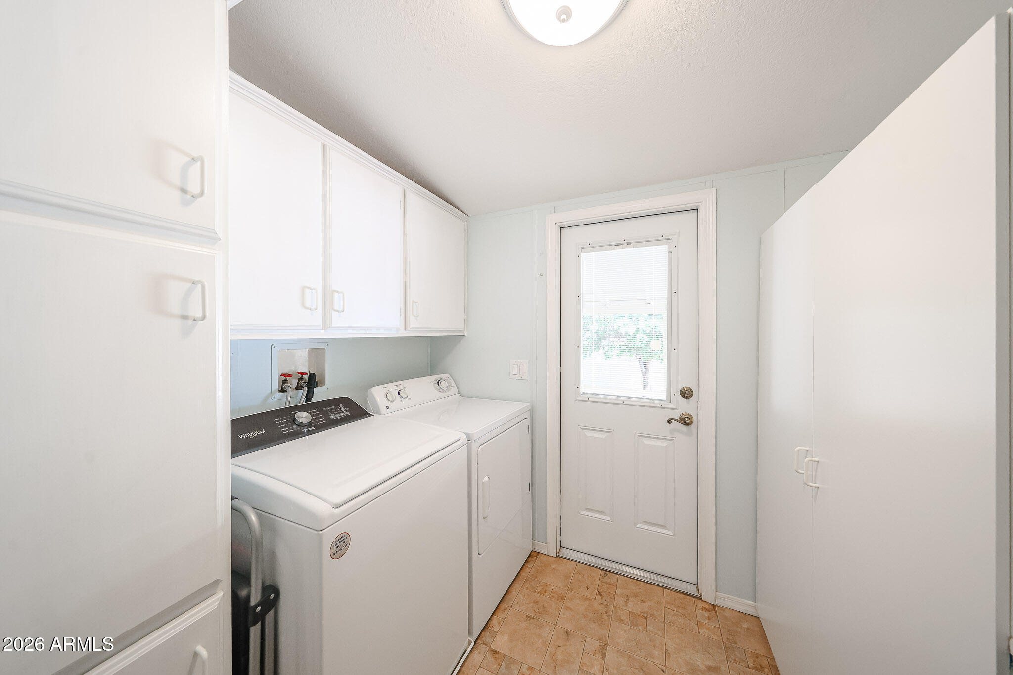 Laundry room with white washer and dryer, upper cabinets, tan tile floor, and a windowed door.