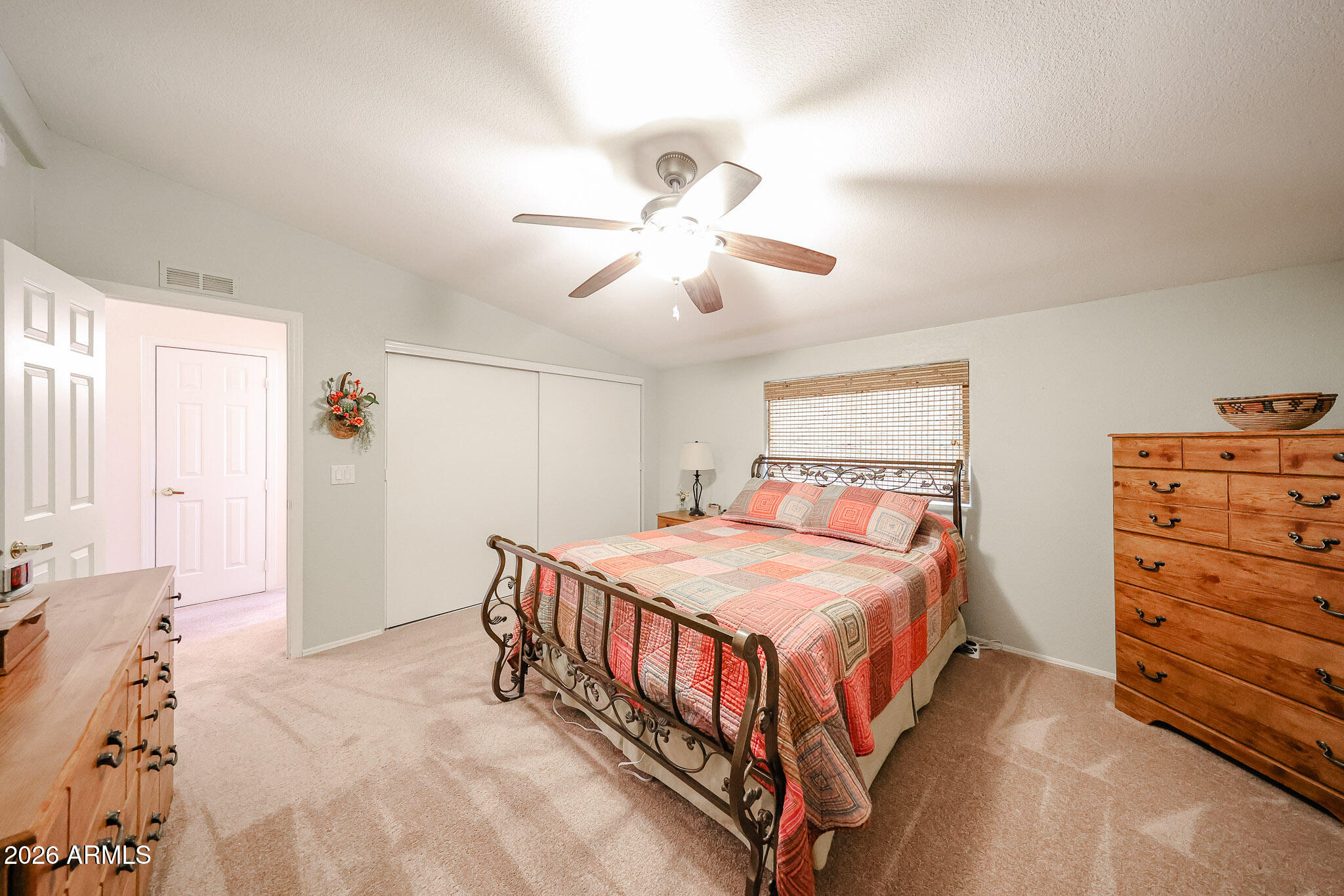 Furnished bedroom with a red patchwork quilt, metal bed frame, ceiling fan, and wooden dressers.