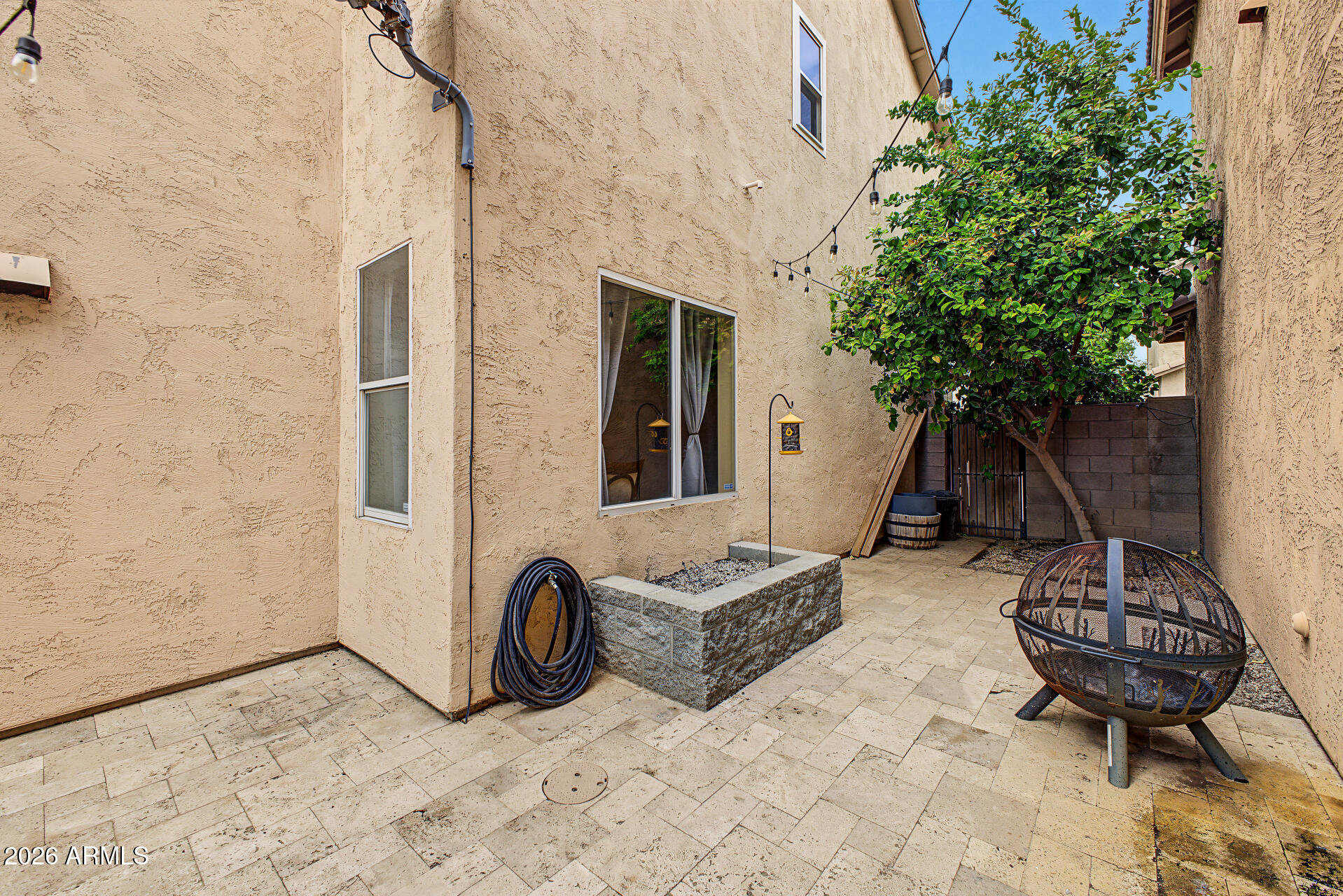 Enclosed tiled courtyard with a leafy tree, string lights, and a metal fire pit.