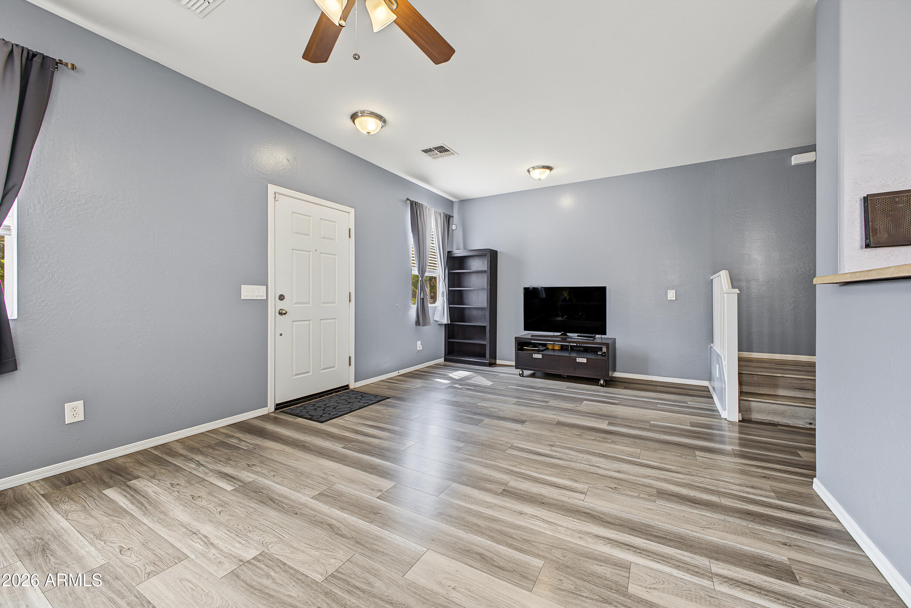 Living room with gray walls, wood-look flooring, a television, and stairs.