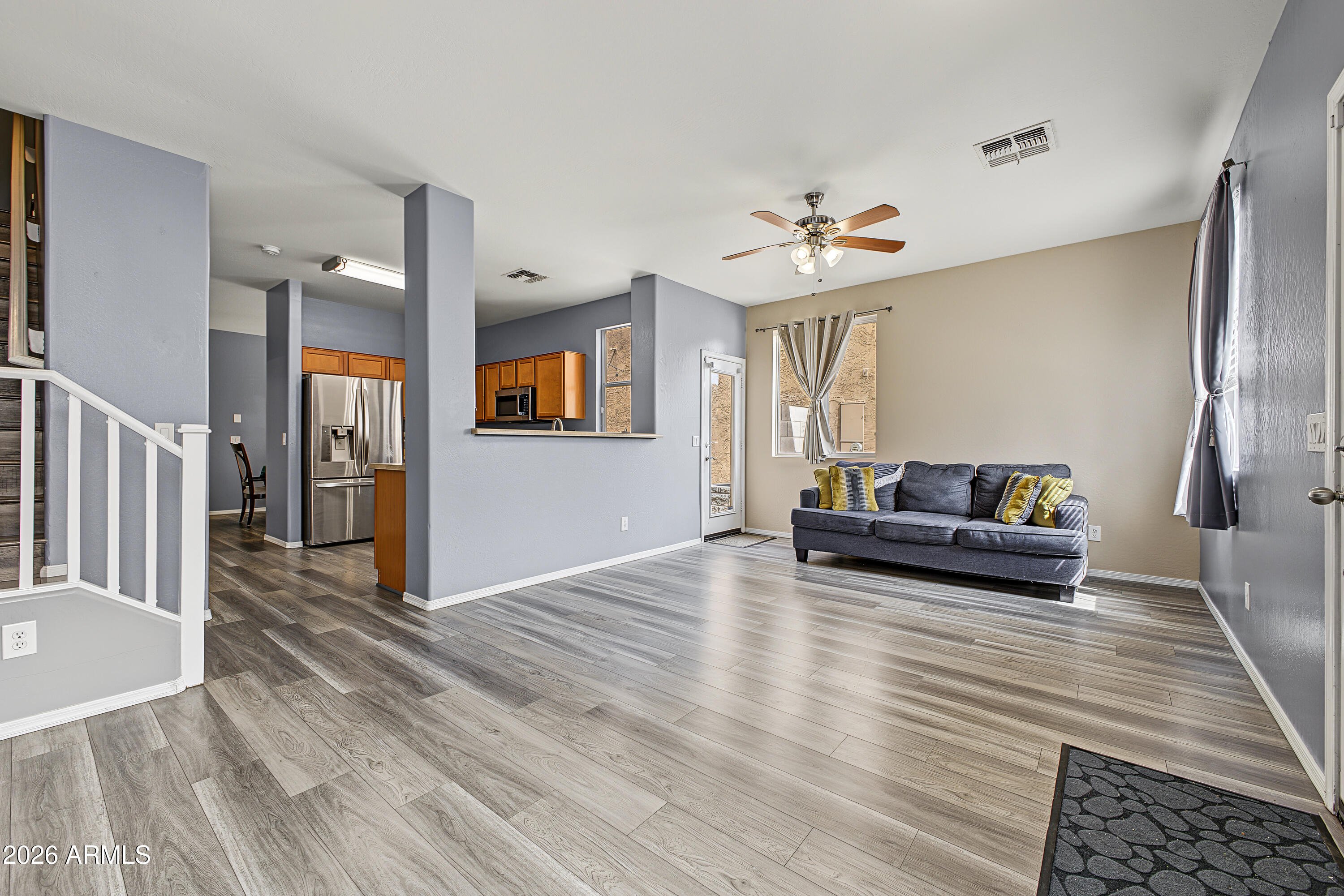 Living room with a dark sofa, wood-look flooring, and an open kitchen with stainless steel appliances.