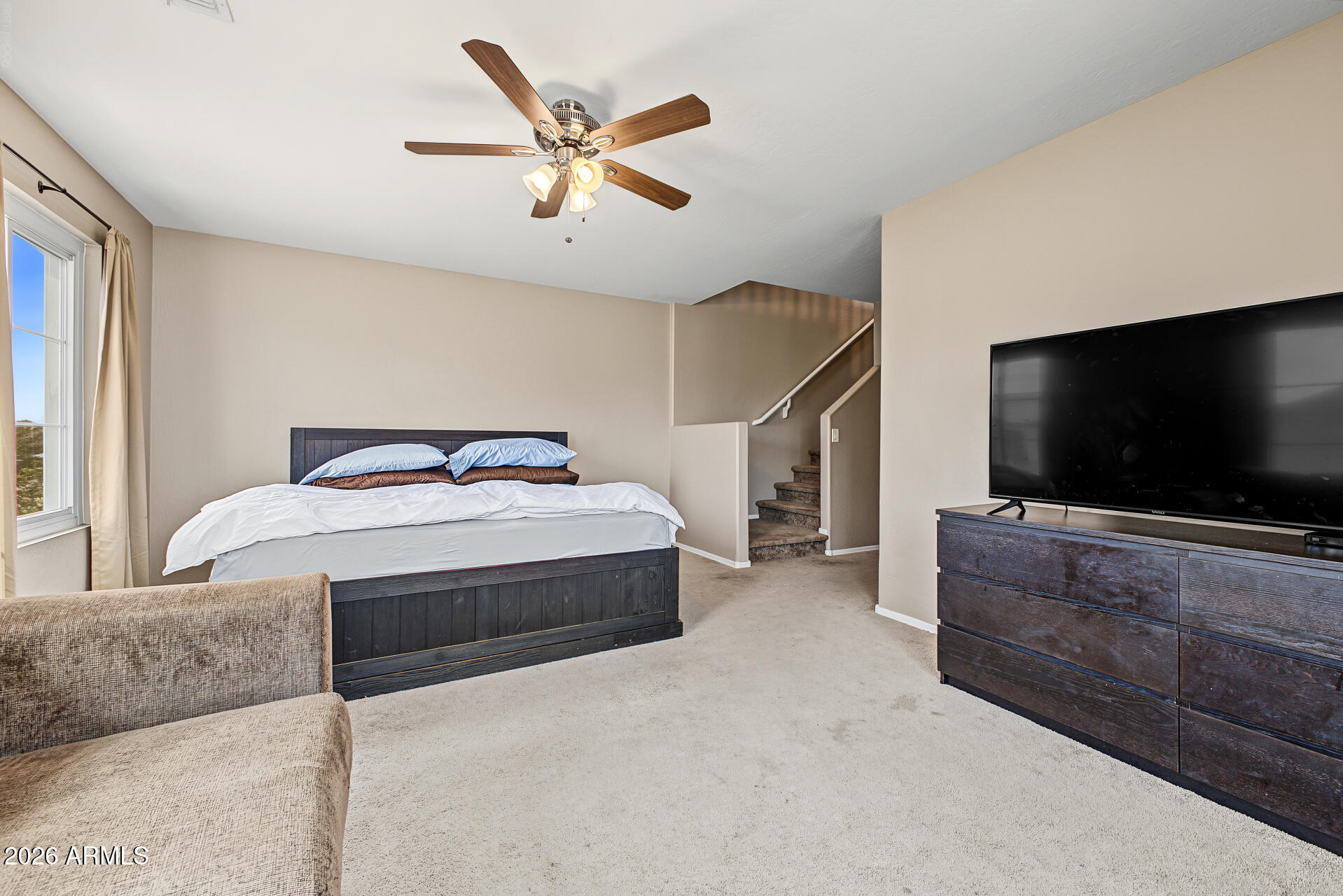 Furnished bedroom with a dark wood bed, ceiling fan, and staircase beside the bed.