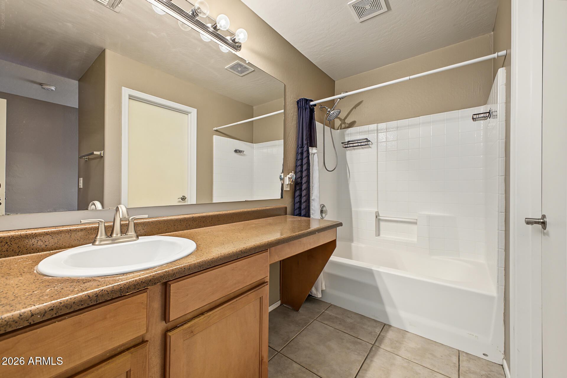 Bathroom with a long speckled vanity, wood cabinets, and a white tub with tiled walls.