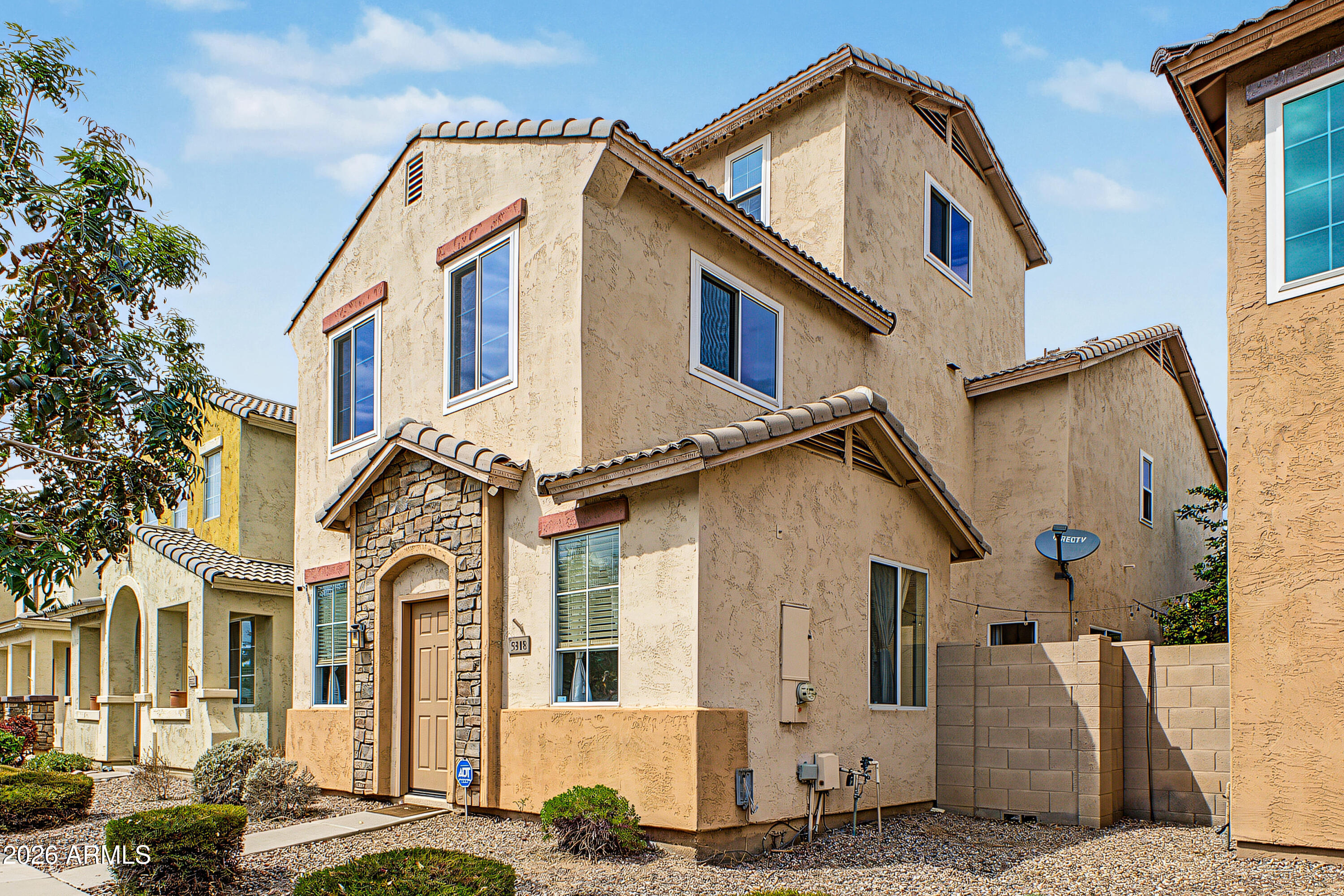 Two-story stucco home with a stone entry surround, tiled roof, and desert landscaping.