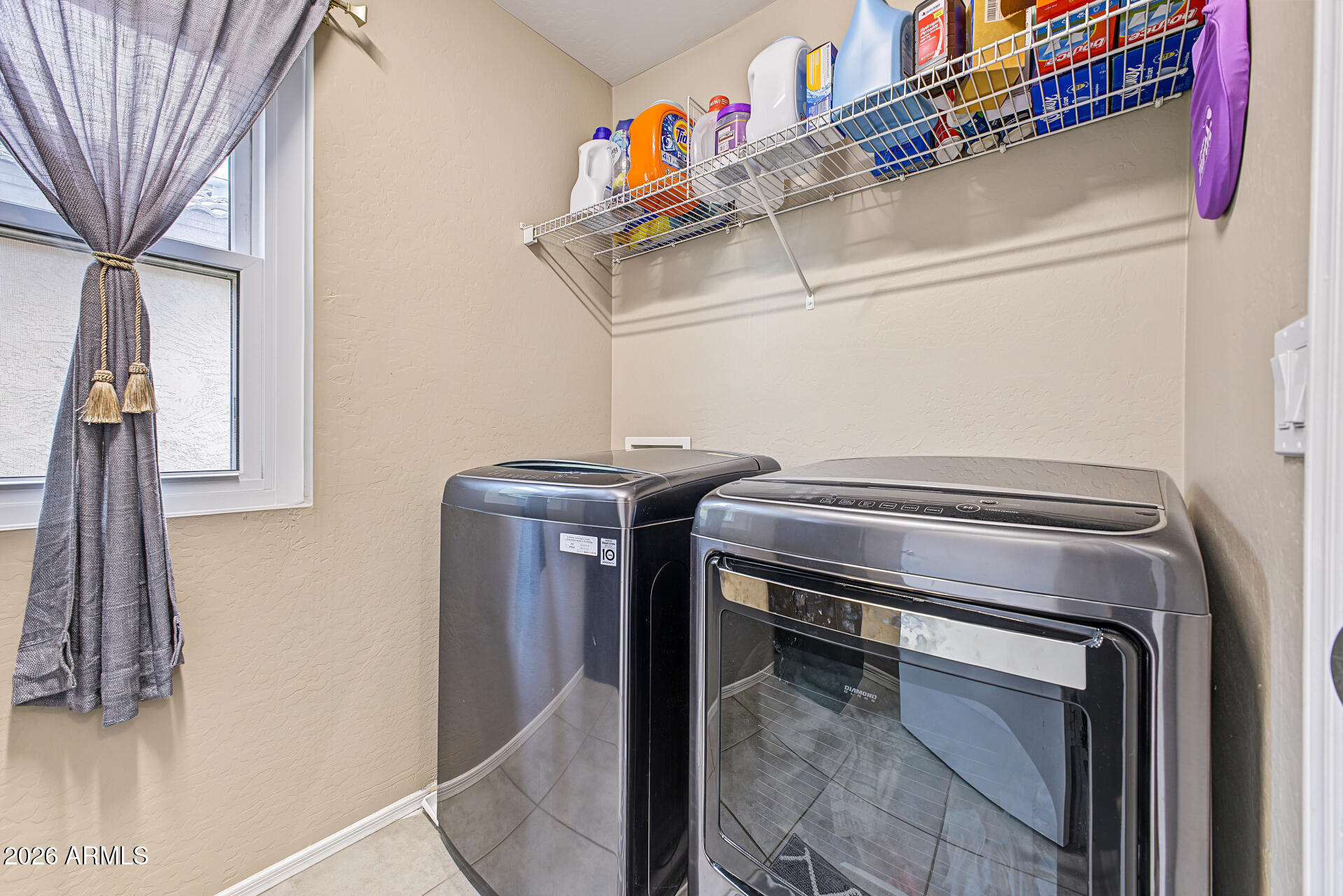 Laundry room with washer and dryer beneath wire shelves stocked with cleaning supplies.