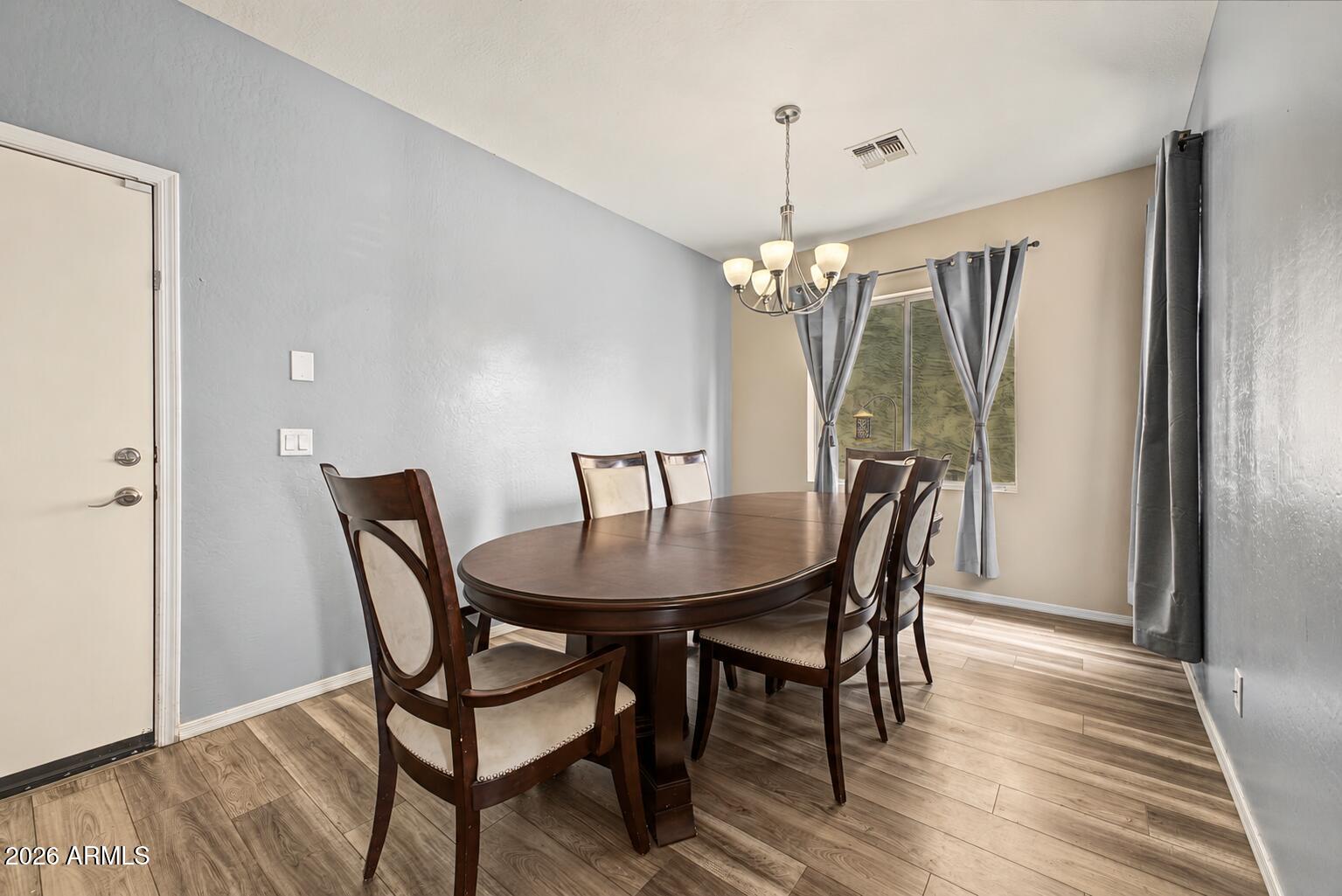 Dining room with an oval dark wood table, upholstered chairs, chandelier, and curtained windows.
