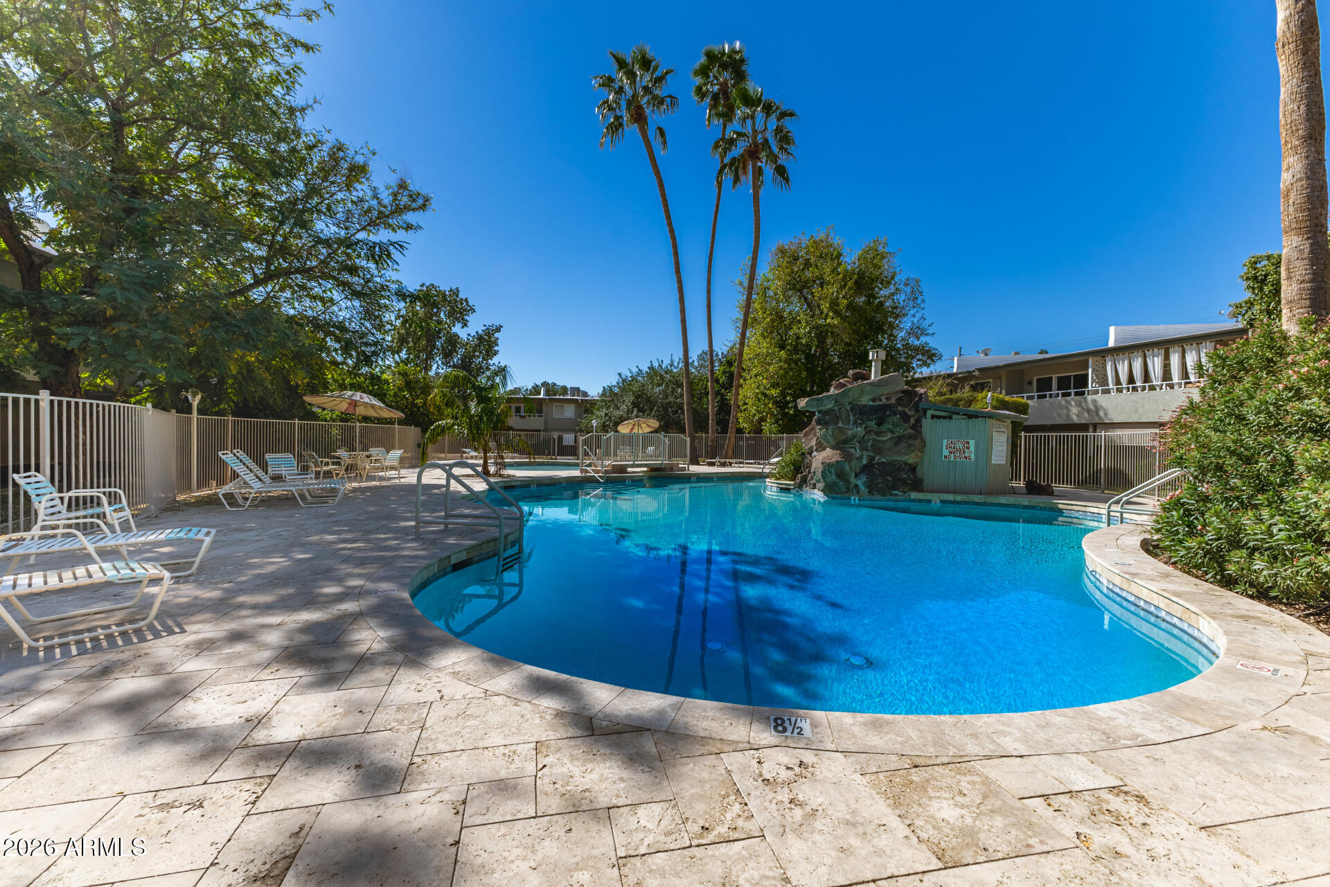 Outdoor pool with a curved edge, rock waterfall, palm trees, and white lounge chairs.