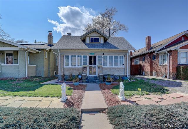 Single-story bungalow with blue-trimmed windows, a covered porch, and two white statues beside the walkway.