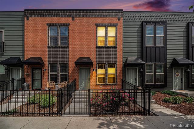 Red-brick townhome with glowing windows and a fenced patio at dusk.