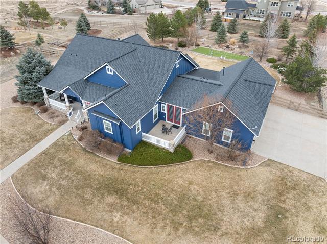 Blue house with a dark roof, white trim, patio, curved lawn, and driveway, seen from above.