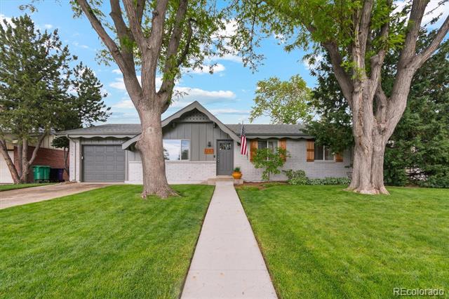 Single-story gray house with a garage, broad green lawn, mature trees, and a walkway to the entrance.