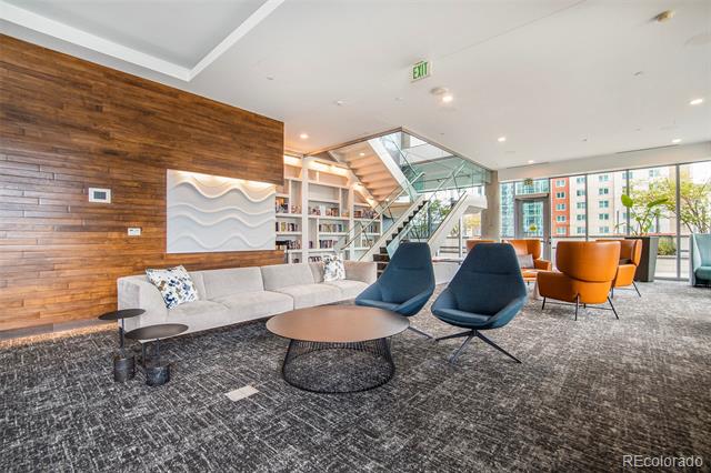 Condo lounge with blue chairs, orange armchairs, a wood accent wall, and a glass-railed staircase.