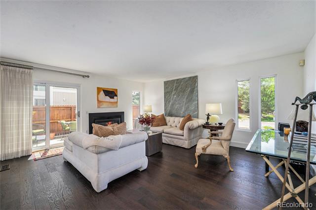 Living room with dark hardwood floors, a fireplace, gray sofas, and large windows opening to a patio.