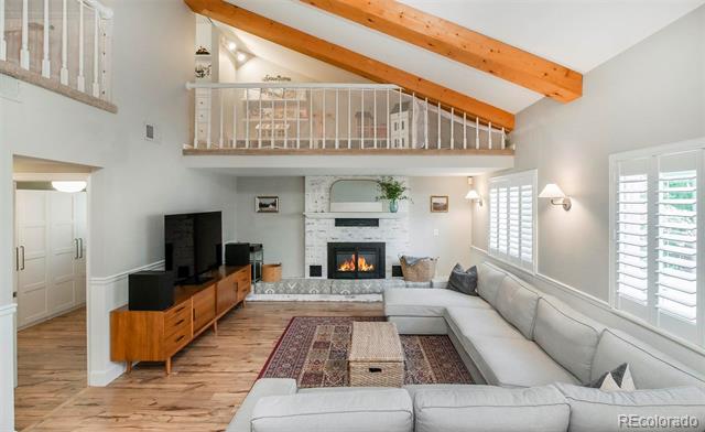 Living room with vaulted ceiling, exposed timber beam, loft railing, stone fireplace, and light sectional sofa.