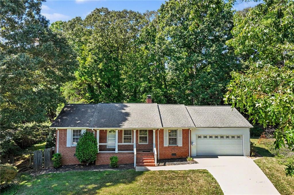 Red-brick ranch home with a covered front porch, attached garage, and wide driveway.