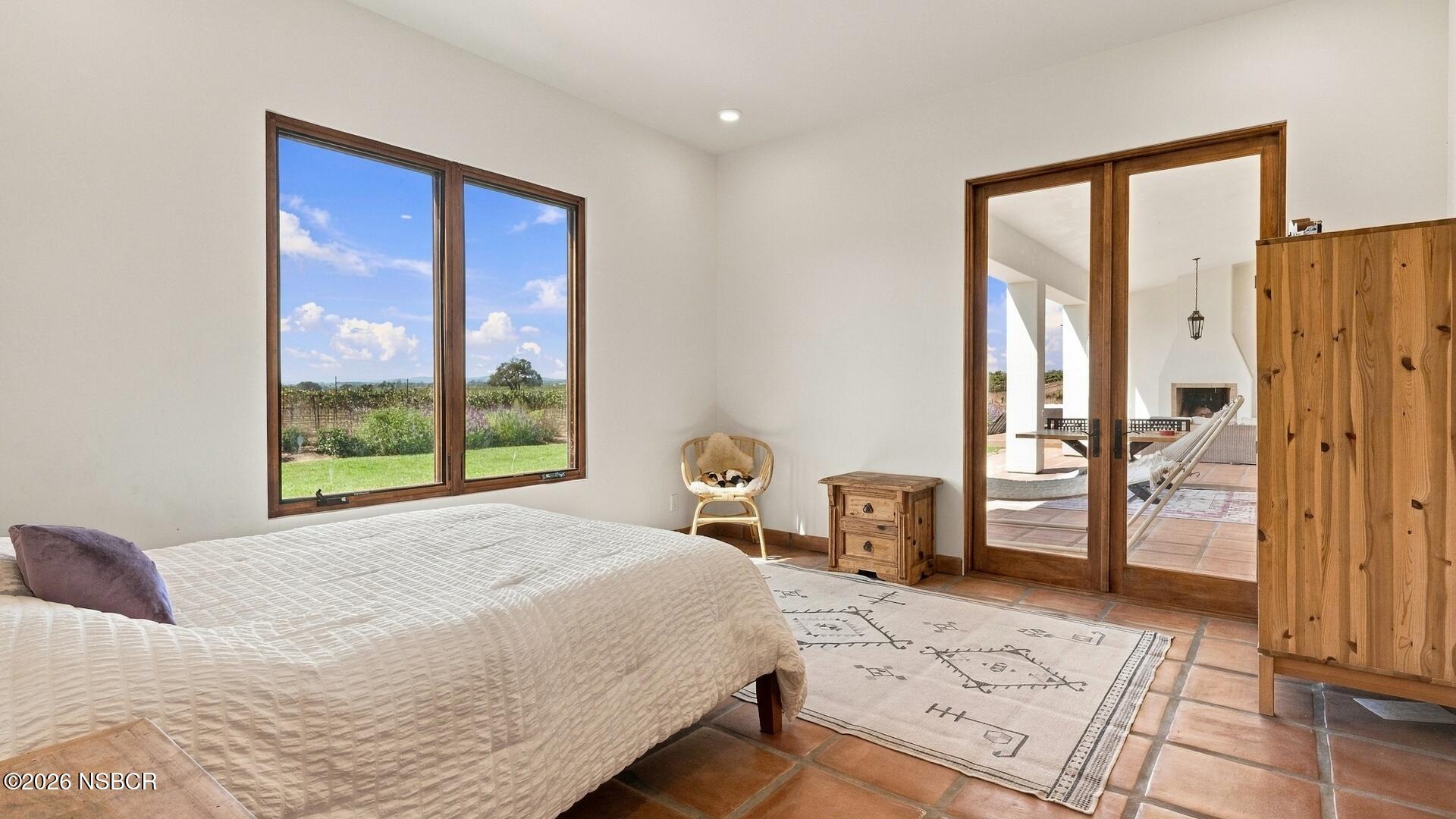 Bedroom with terracotta tile floors, vineyard views, and glass doors opening to a covered patio.