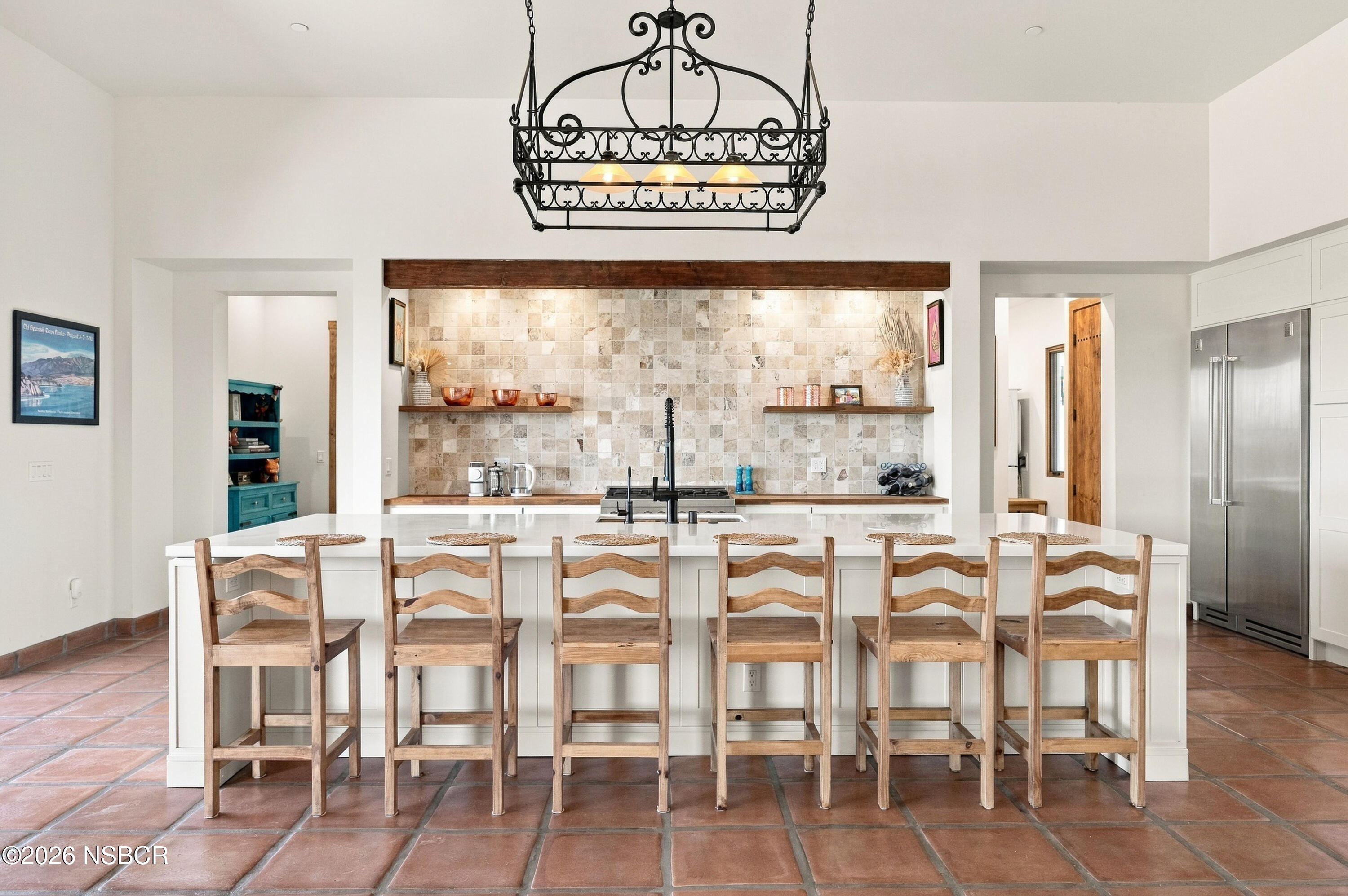 Kitchen with a white island, six wooden chairs, terracotta tile floors, and an ornate iron chandelier.