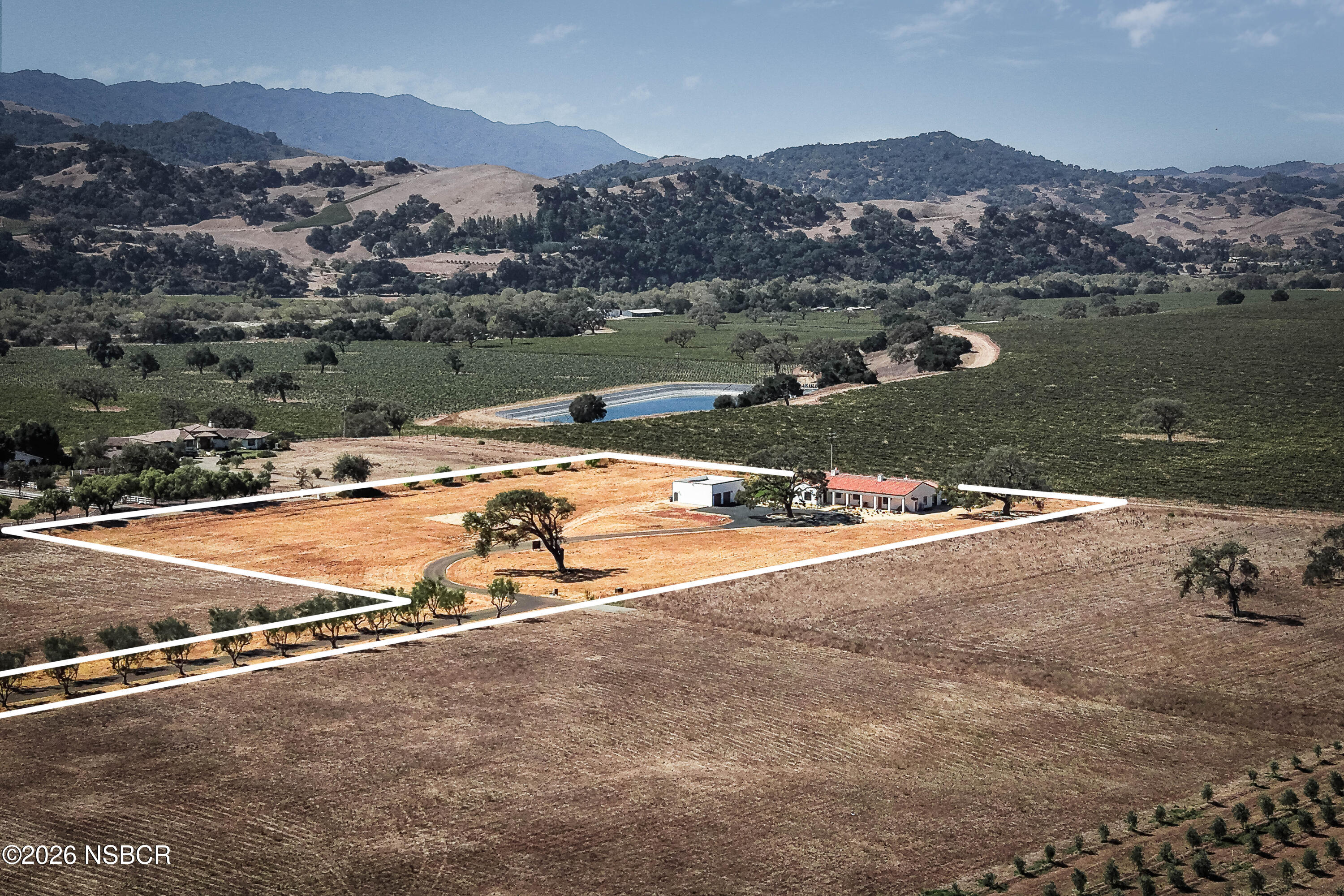 Aerial view of a rural property outlined in white, with a red-roofed home, outbuilding, and vineyard nearby.
