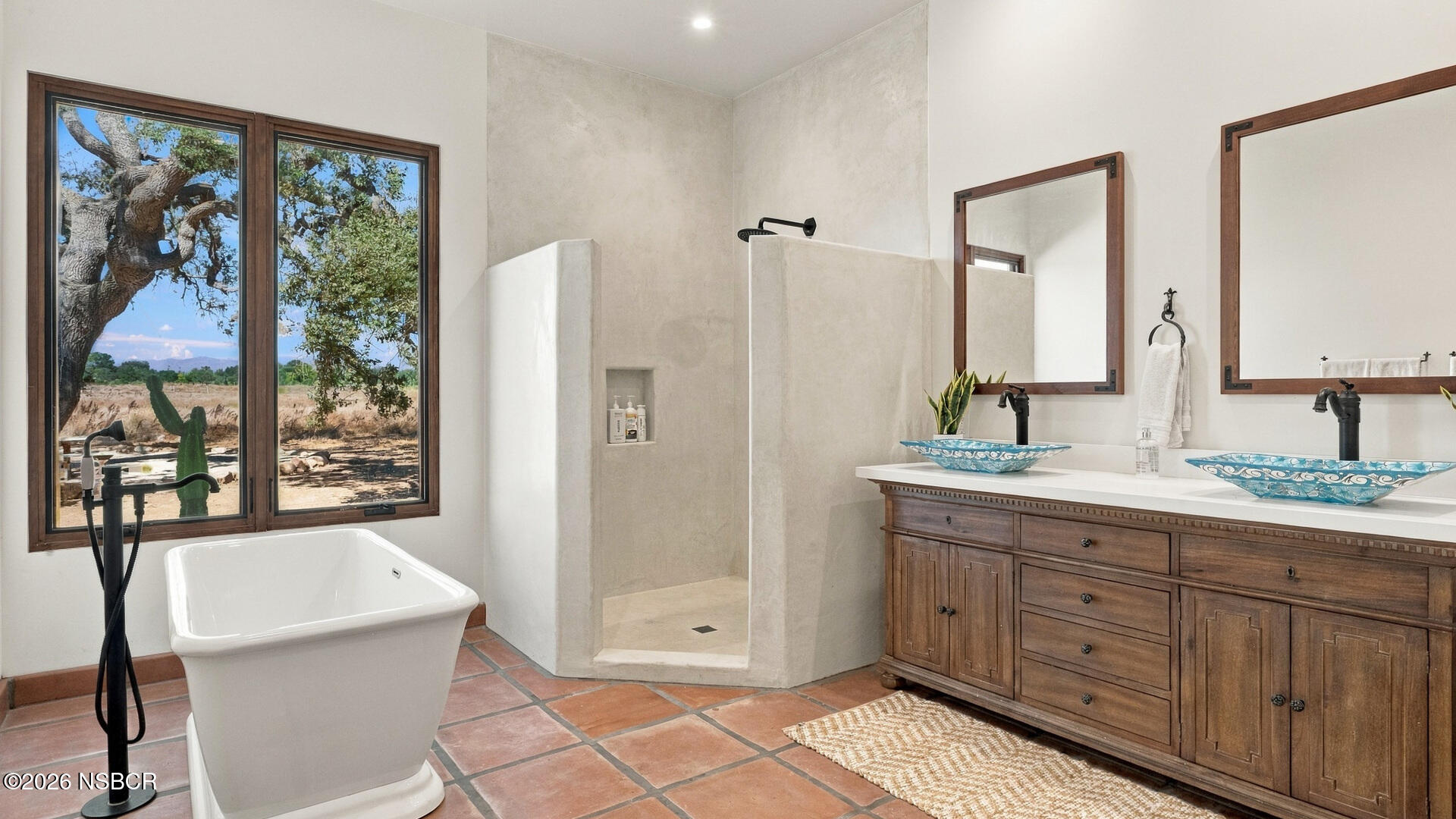 Bathroom with a walk-in shower, freestanding tub, and double vanity overlooking oak-dotted land.