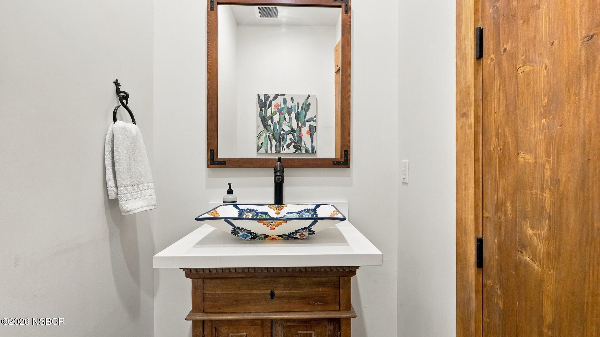 Bathroom vanity with a colorful floral vessel sink, dark faucet, and wooden cabinet.