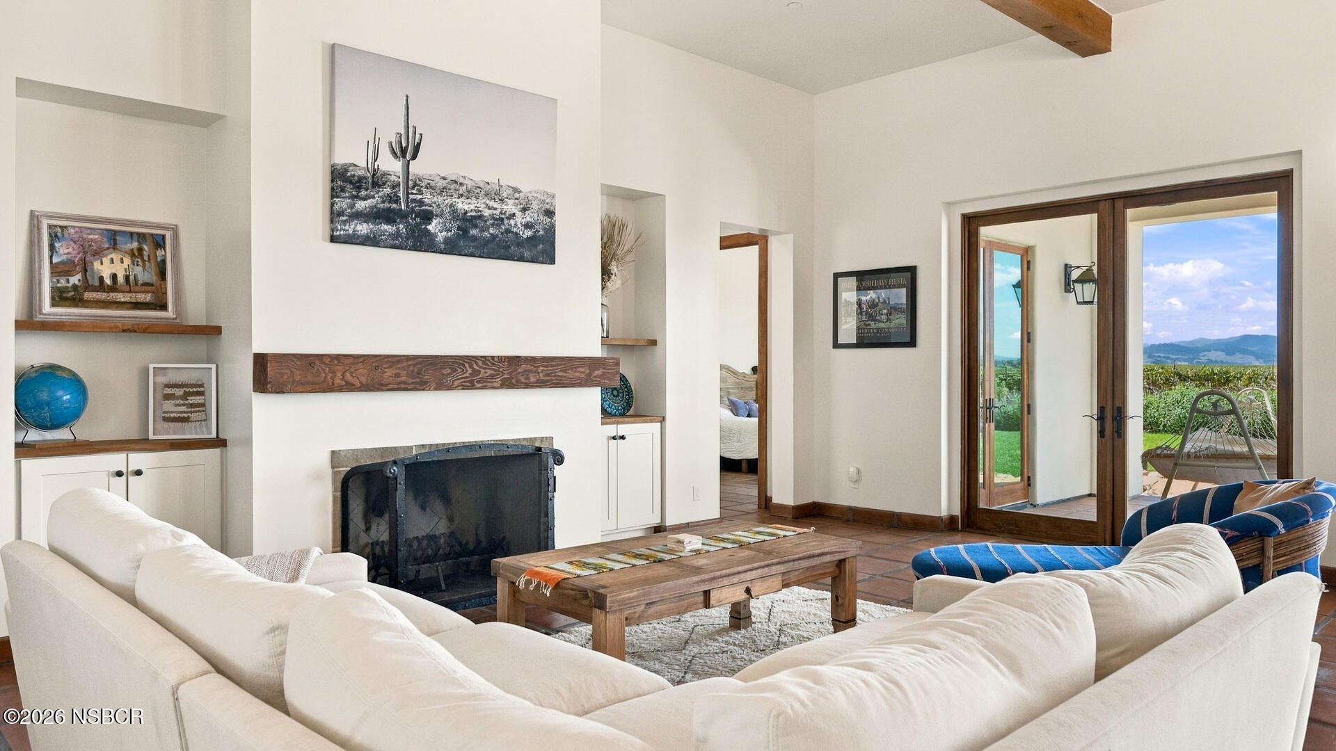 Living room with a large fireplace, white sofas, and French doors overlooking a vineyard and mountains.