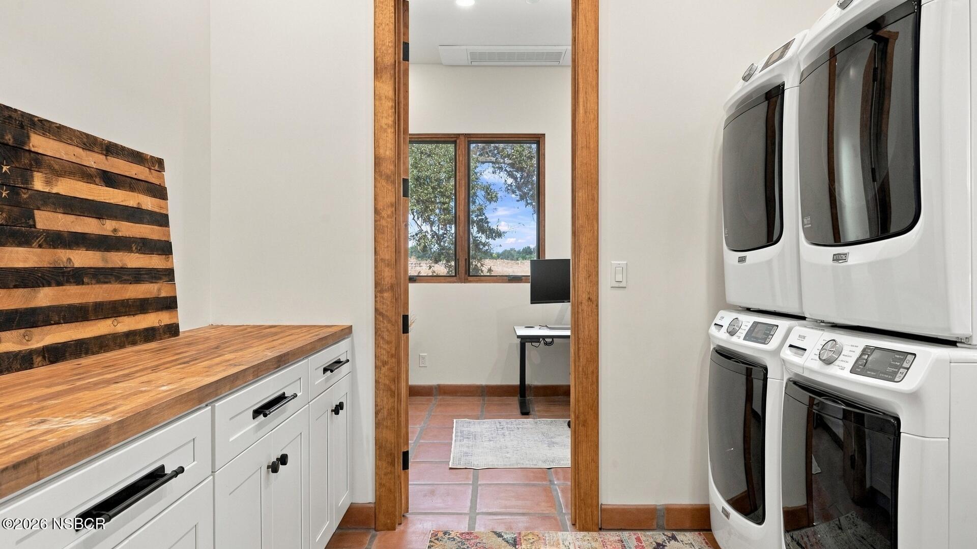 Laundry room with paired white washer-dryers and a wood countertop beside an open doorway.