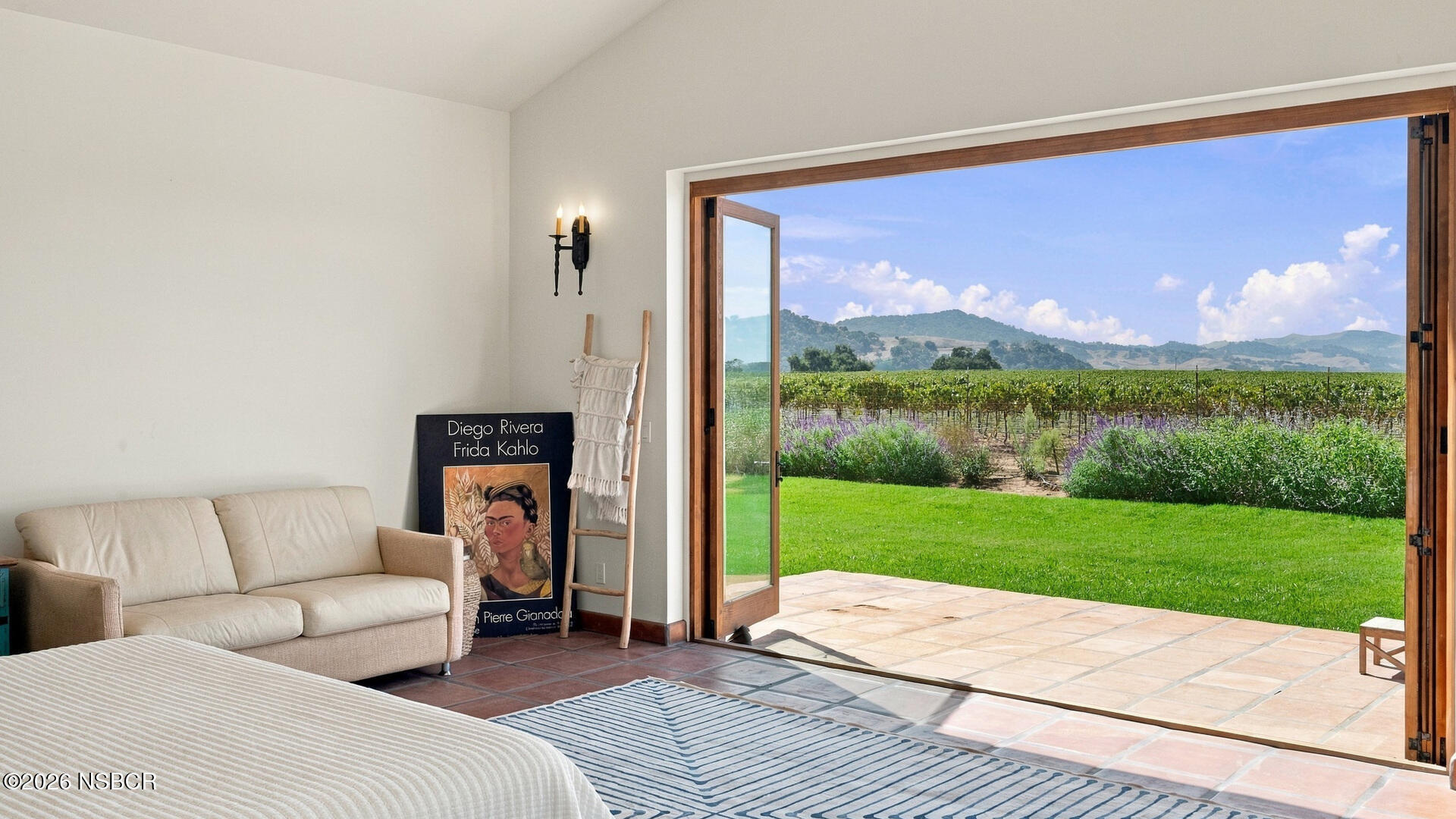 Bedroom with open doors overlooking a vineyard, lawn, and rolling hills.