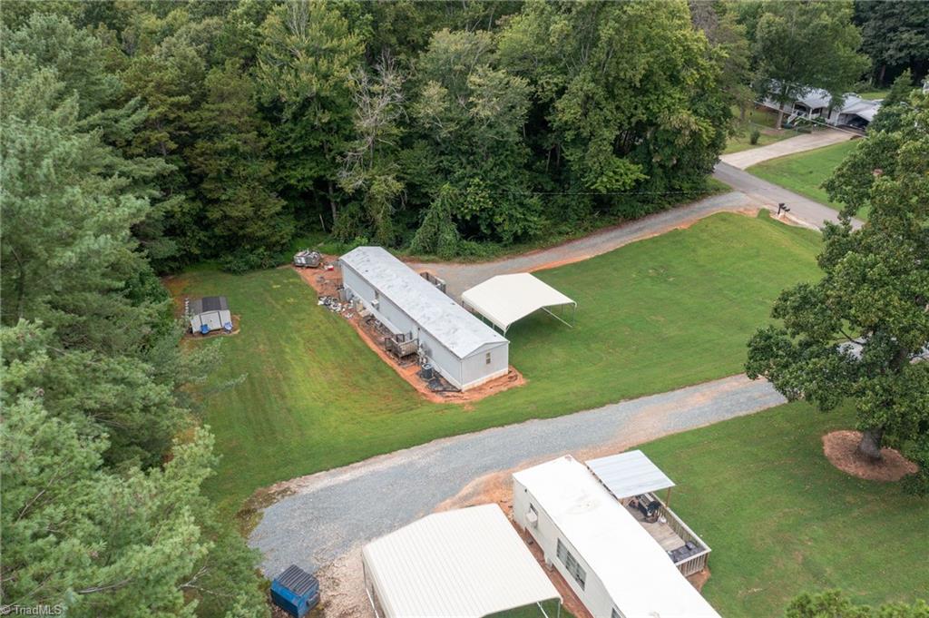 Aerial view of a long building and open-sided carport on a grassy, wooded property.