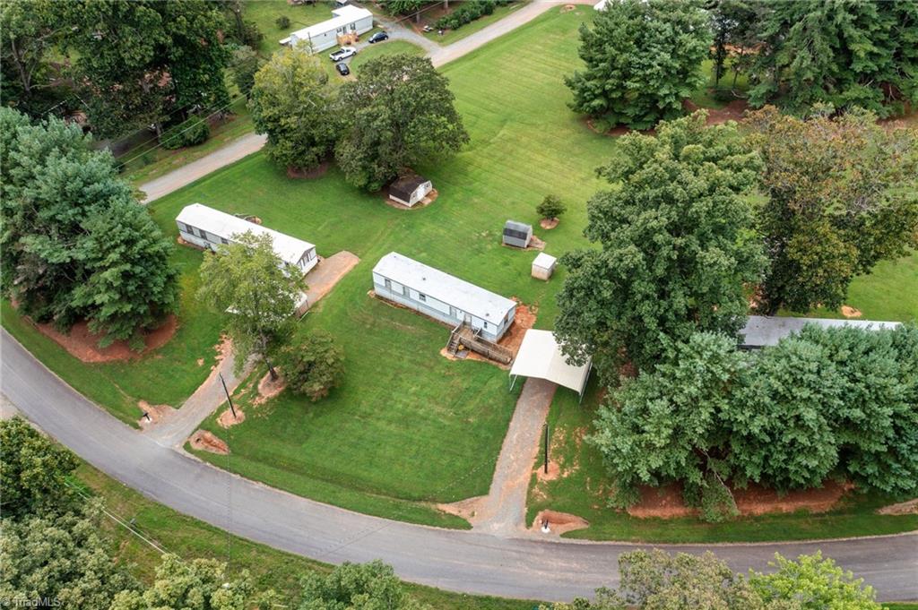 Aerial view of several manufactured homes on a grassy, tree-lined lot beside a road.