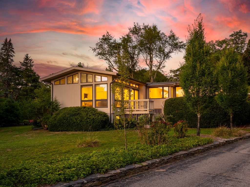 Modern home with warmly lit windows and a small deck beneath a pink sunset.