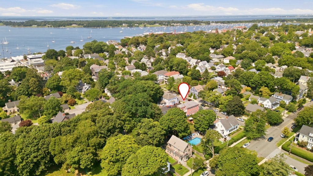 Aerial view of a coastal neighborhood home marked by a pin, with a sailboat-filled bay beyond.