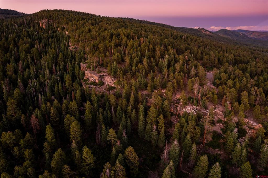 Aerial view of forested mountain land with rocky outcrops beneath a pink dusk sky.