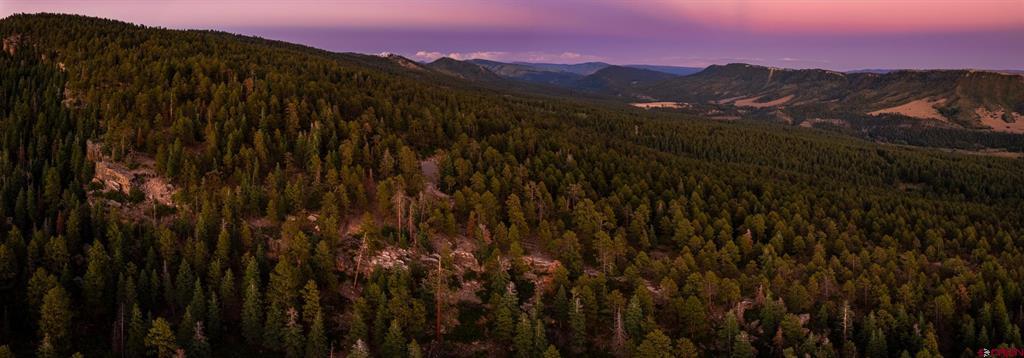 Wooded mountain land overlooking distant ridges beneath a pink dusk sky.