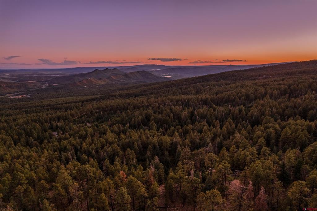 Aerial view of forested mountain land and distant ridges beneath a colorful dusk sky.