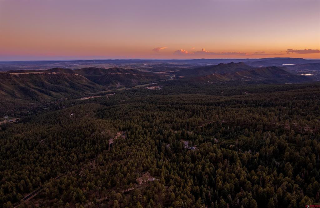 Aerial view of forested mountain terrain and distant ridgelines beneath a pink dusk sky.