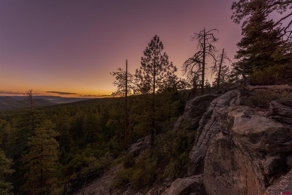 Rocky, pine-covered hillside overlooking distant ridges beneath a purple and orange dusk sky.