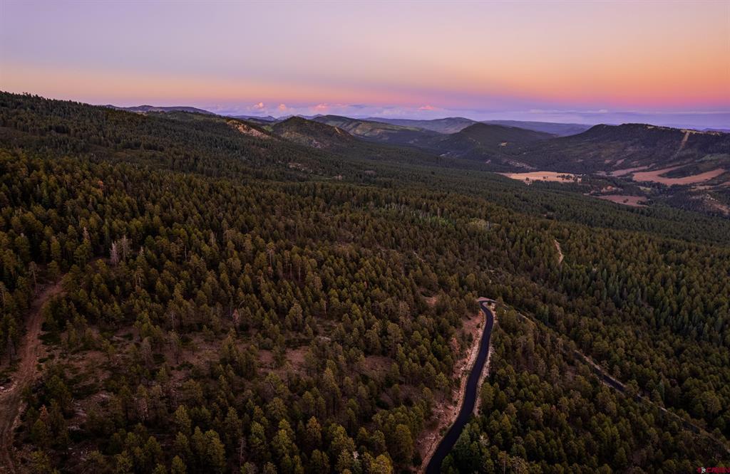 Aerial view of forested mountain land with a winding road beneath a pink dusk sky.