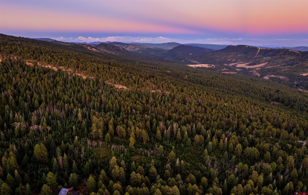 Aerial view across forested hills and distant mountains beneath a pink dusk sky.