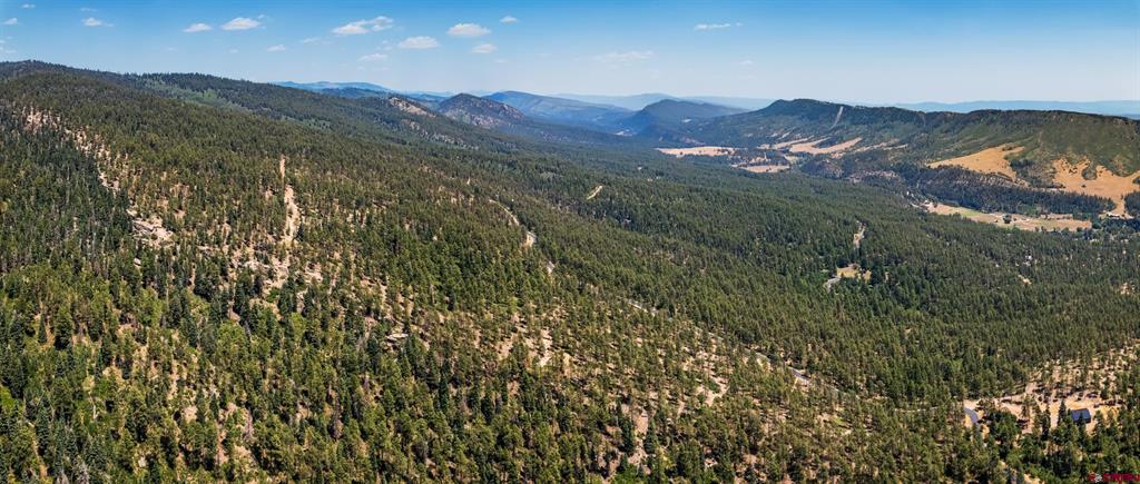 Aerial view of a forested mountain property overlooking a broad valley and distant ridgelines.