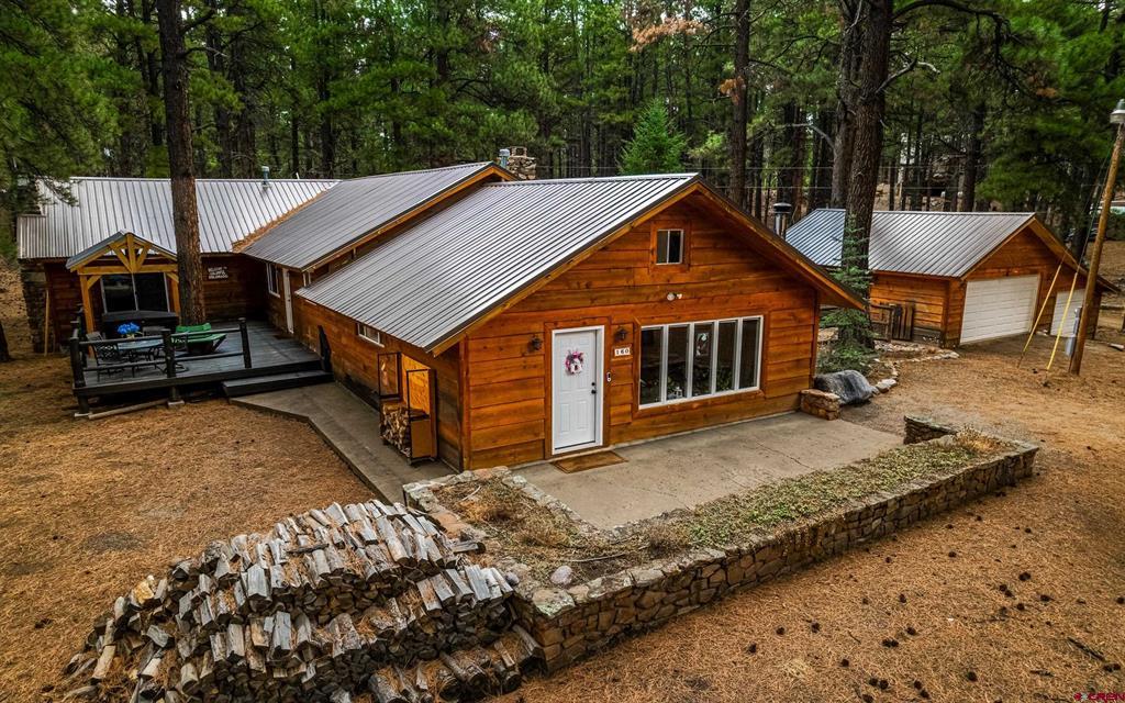 Rustic wood-sided home with a metal roof, covered deck, detached garage, and wooded surroundings.
