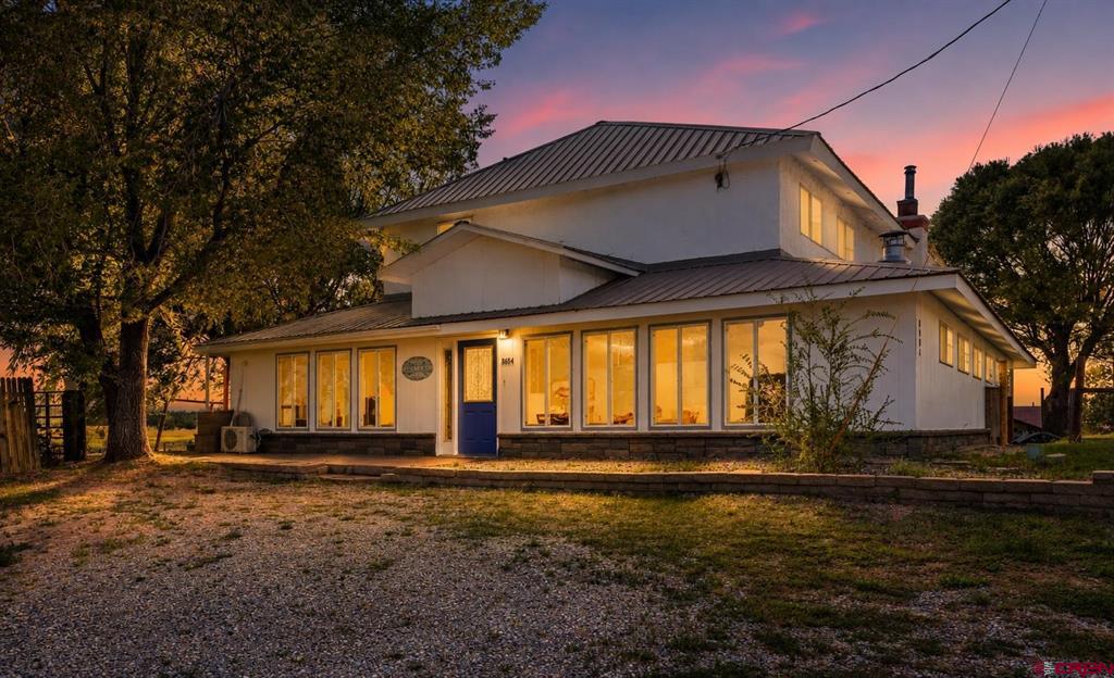 White two-story home with a blue front door and warmly lit windows at dusk.