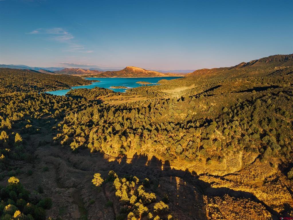 Aerial view of a turquoise lake among golden forested hills and distant mountains.