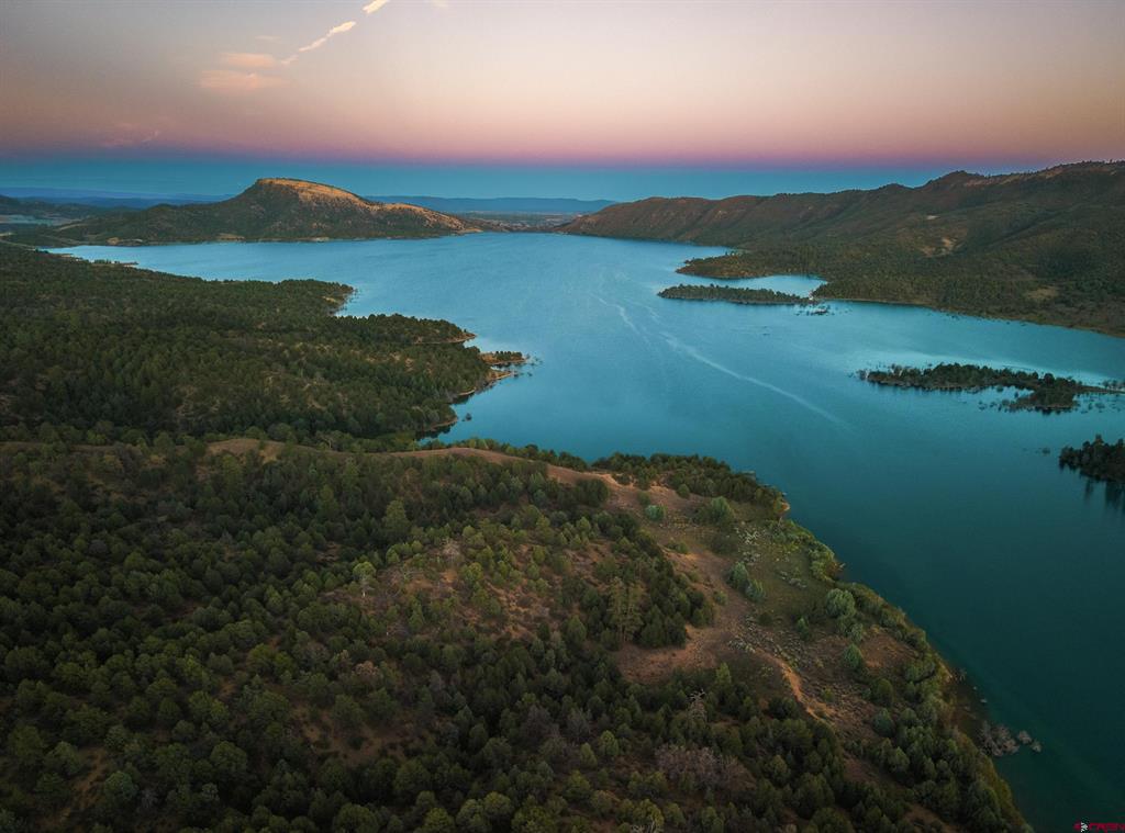 Aerial view of a blue lake winding between forested shorelines and hills at dusk.