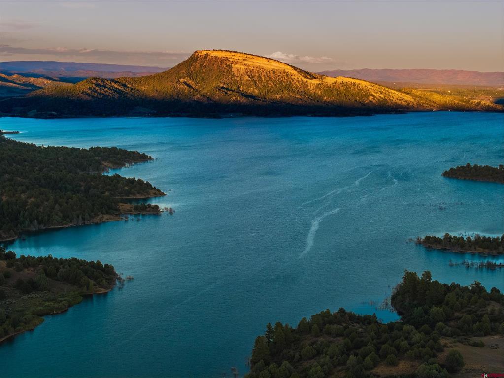 Aerial lake view with wooded shorelines and a golden-lit mountain ridge.
