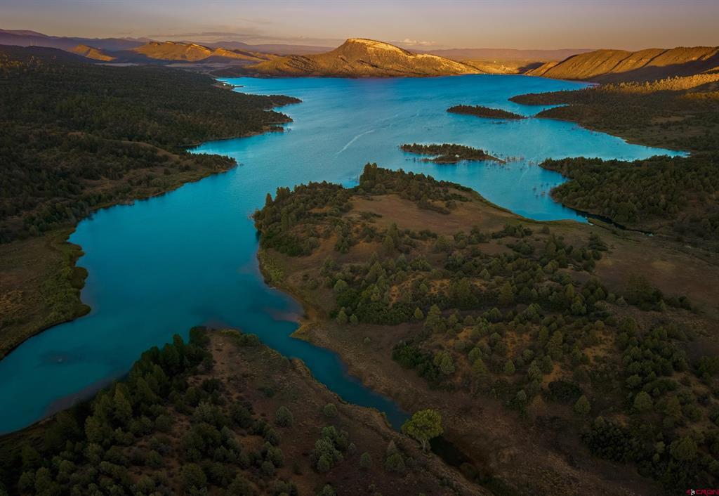 Turquoise lake winds through forested hills beneath sunlit mountain ridges.
