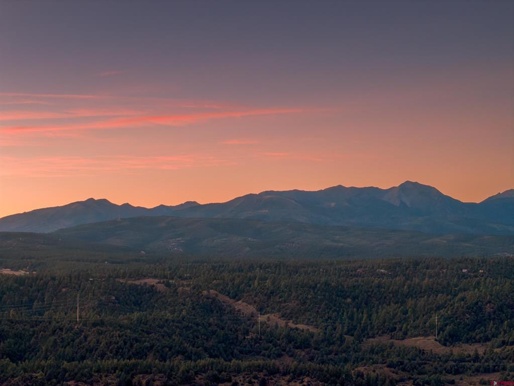 Mountain range and forested foothills beneath a pink-orange sunset sky.