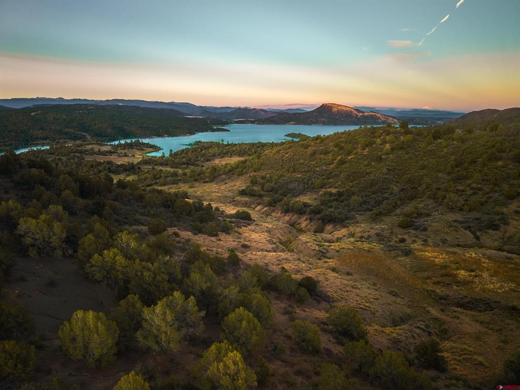 Aerial view of a lake amid wooded hills and mountains at sunset.