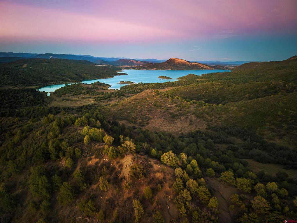 Turquoise lake among forested hills at sunset, viewed from above.