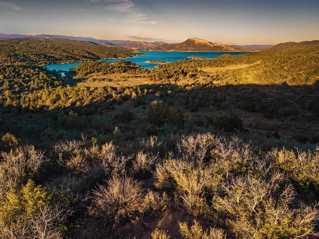 Aerial panorama of a turquoise lake among forested hills and distant mountains.